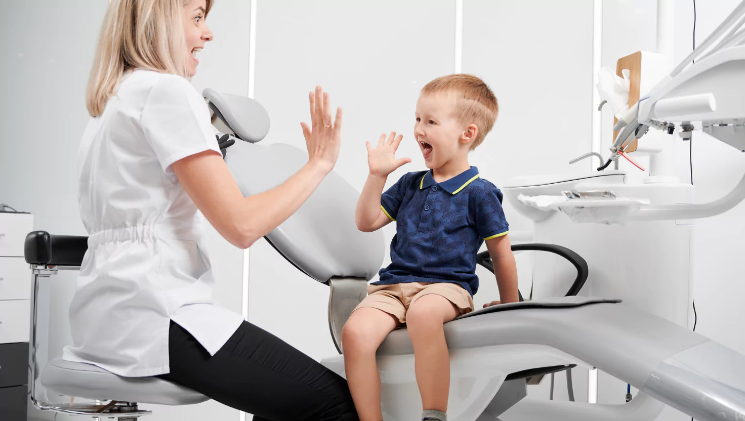 A child in a dentist’s chair laughing or high-fiving the dentist.